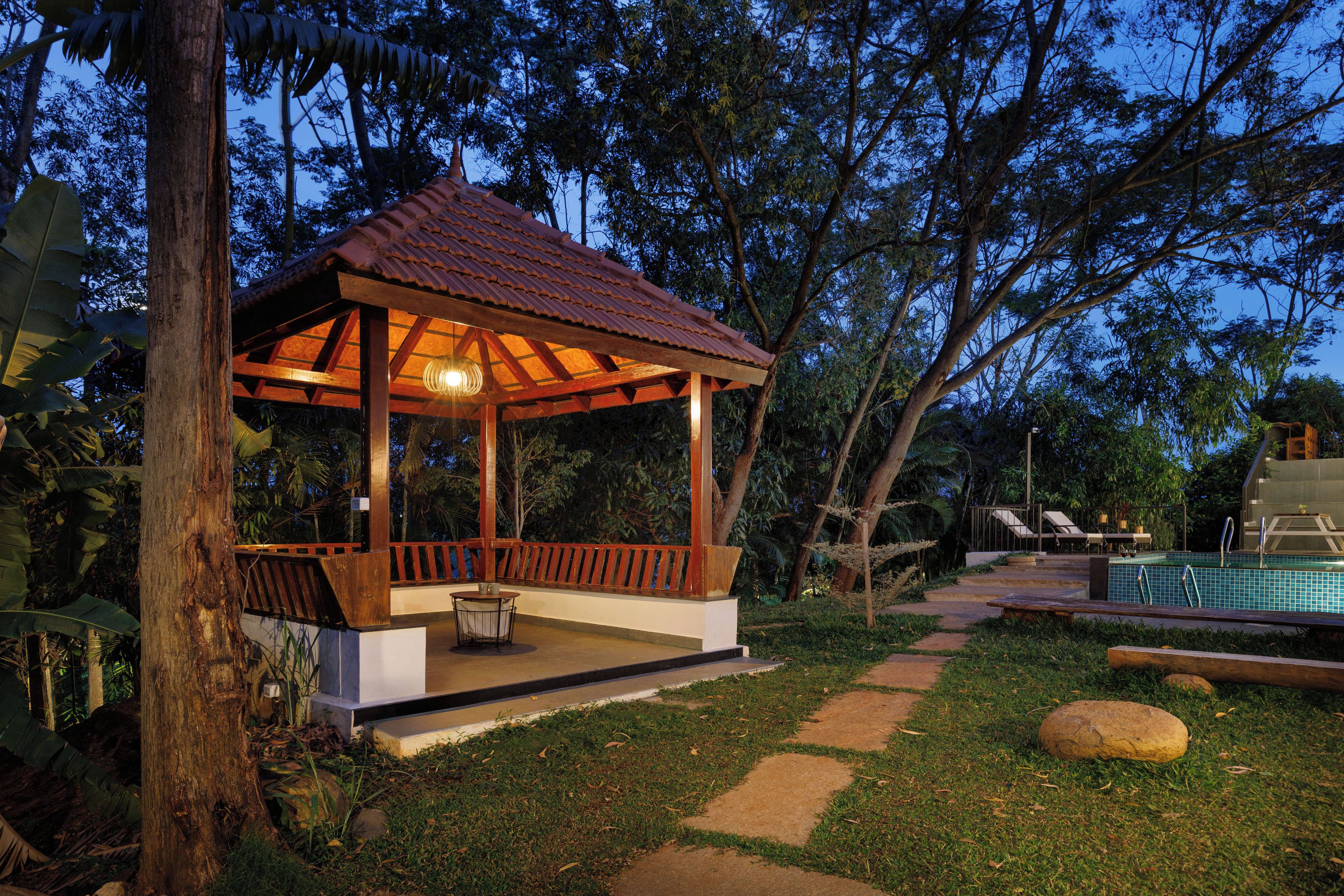 Um gazebo com telhado de azulejos, cercado por uma piscina e espreguiçadeiras.