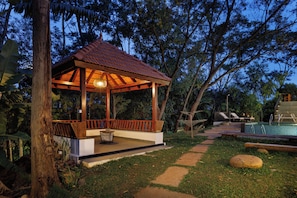 A gazebo with a tiled roof, surrounded by a pool and lounge chairs.