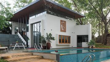 Una casa moderna con piscina, una escalera y un gran árbol al fondo.