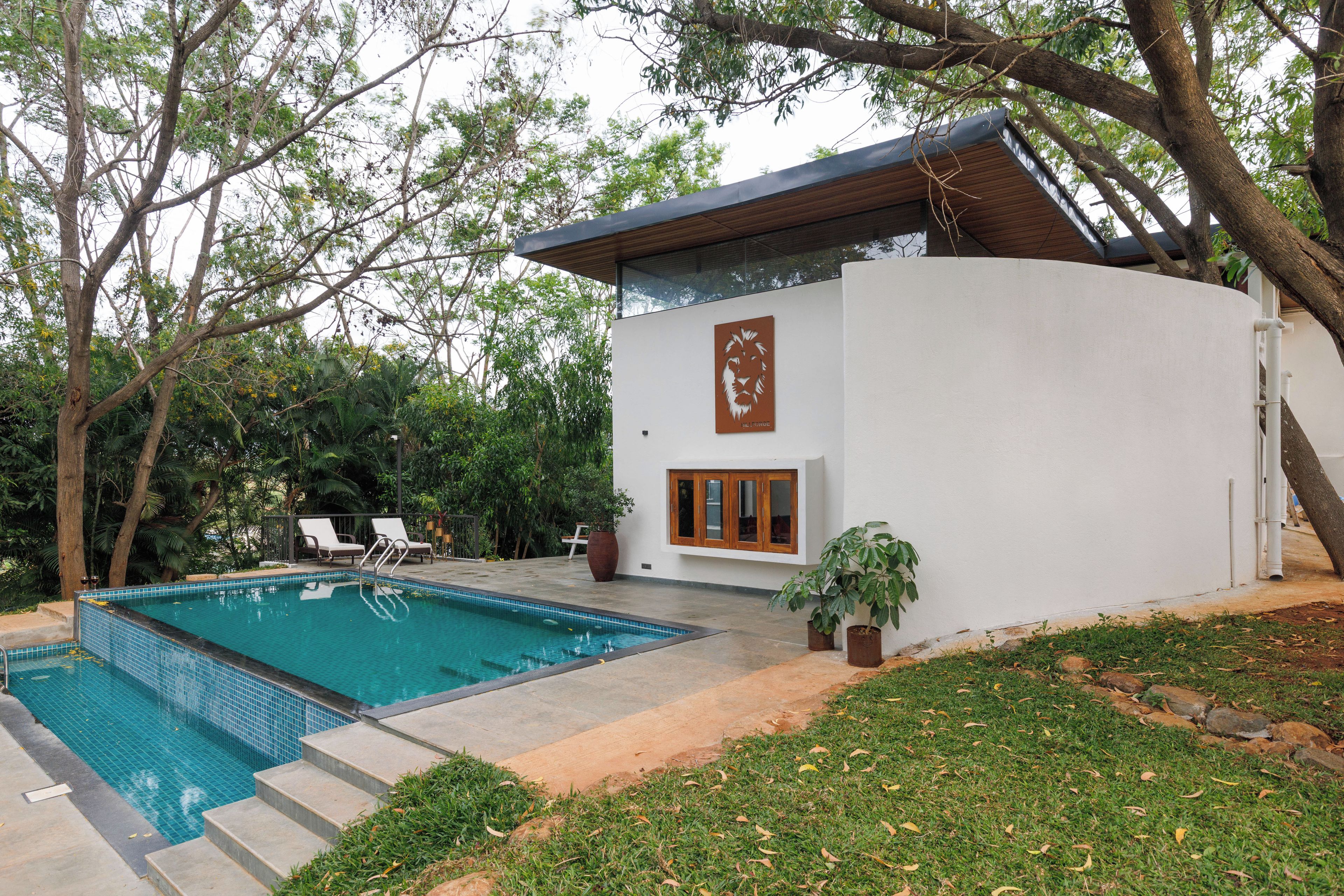 Una casa moderna con piscina, un patio con sillas y un árbol grande.