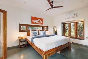 A bedroom with a wooden bed, a nightstand, a ceiling fan, a window with blinds, and a wall-mounted air conditioner.