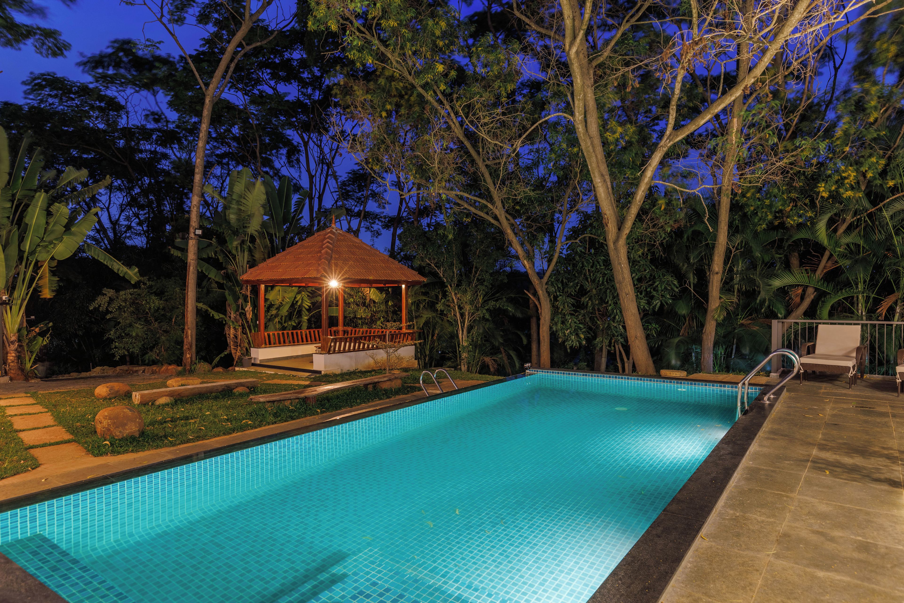 Una piscina con un pabellón y sillas de descanso, rodeada de vegetación tropical.