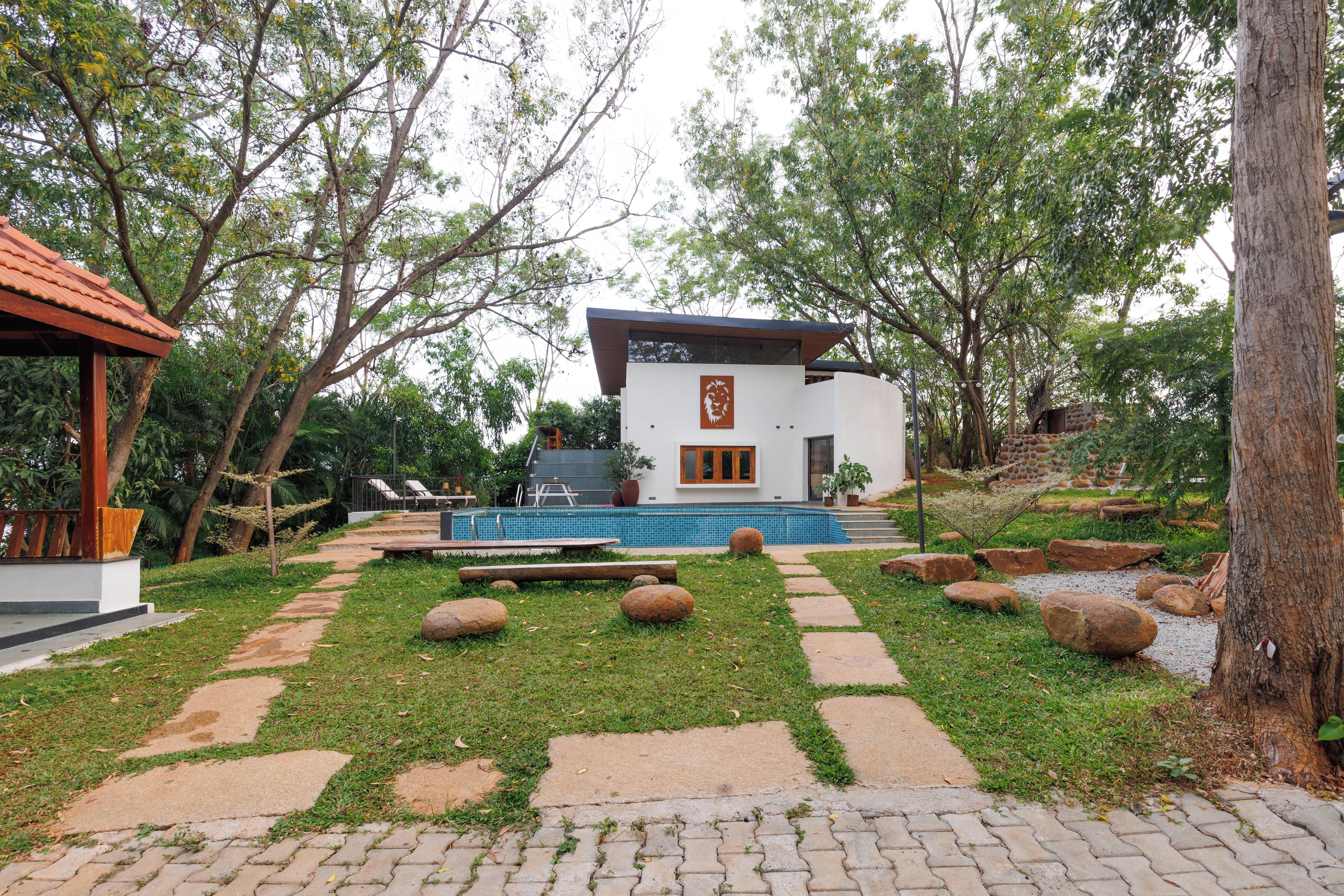Un edificio moderno con piscina, rodeado de árboles y un sendero de piedra.