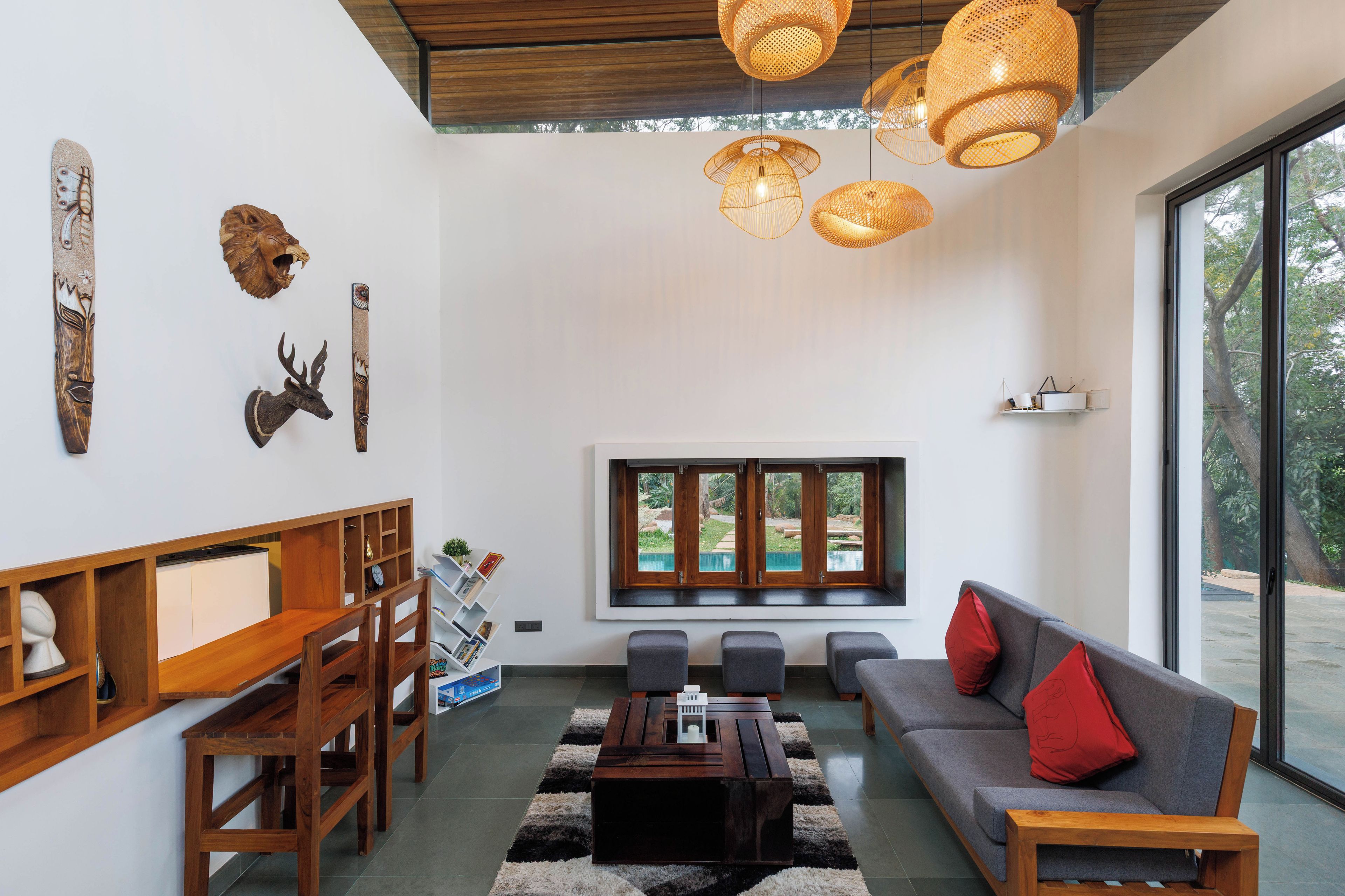 Una sala de estar moderna con sofá, mesa de centro y sillas, un comedor con mesa y sillas de madera, y un ventanal con vista a una piscina y follaje.