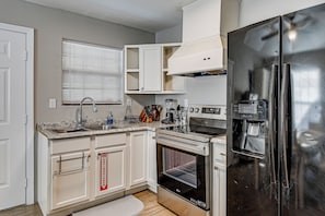 A kitchen with white cabinets, a stainless steel refrigerator, a built-in oven, and a window with blinds.