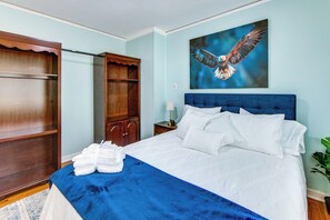 A bedroom with a large bed, a wooden wardrobe, a nightstand with a lamp, and a painting of an eagle.