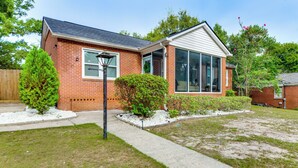 Une maison à deux étages, avec une façade en briques, une grande fenêtre et un jardin visible à l’avant, comprenant une pelouse et un petit arbre.