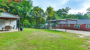 Un jardin à l’arrière d’une maison, avec une terrasse couverte, une pelouse et un bâtiment en briques.