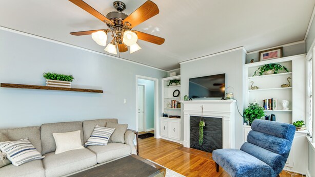Un salon comprenant un canapé, un fauteuil bleu, une table basse, une cheminée, un téléviseur et un ventilateur de plafond.