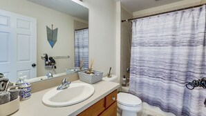 Une salle de bain avec un lavabo blanc, un miroir, des toilettes et un rideau de douche.