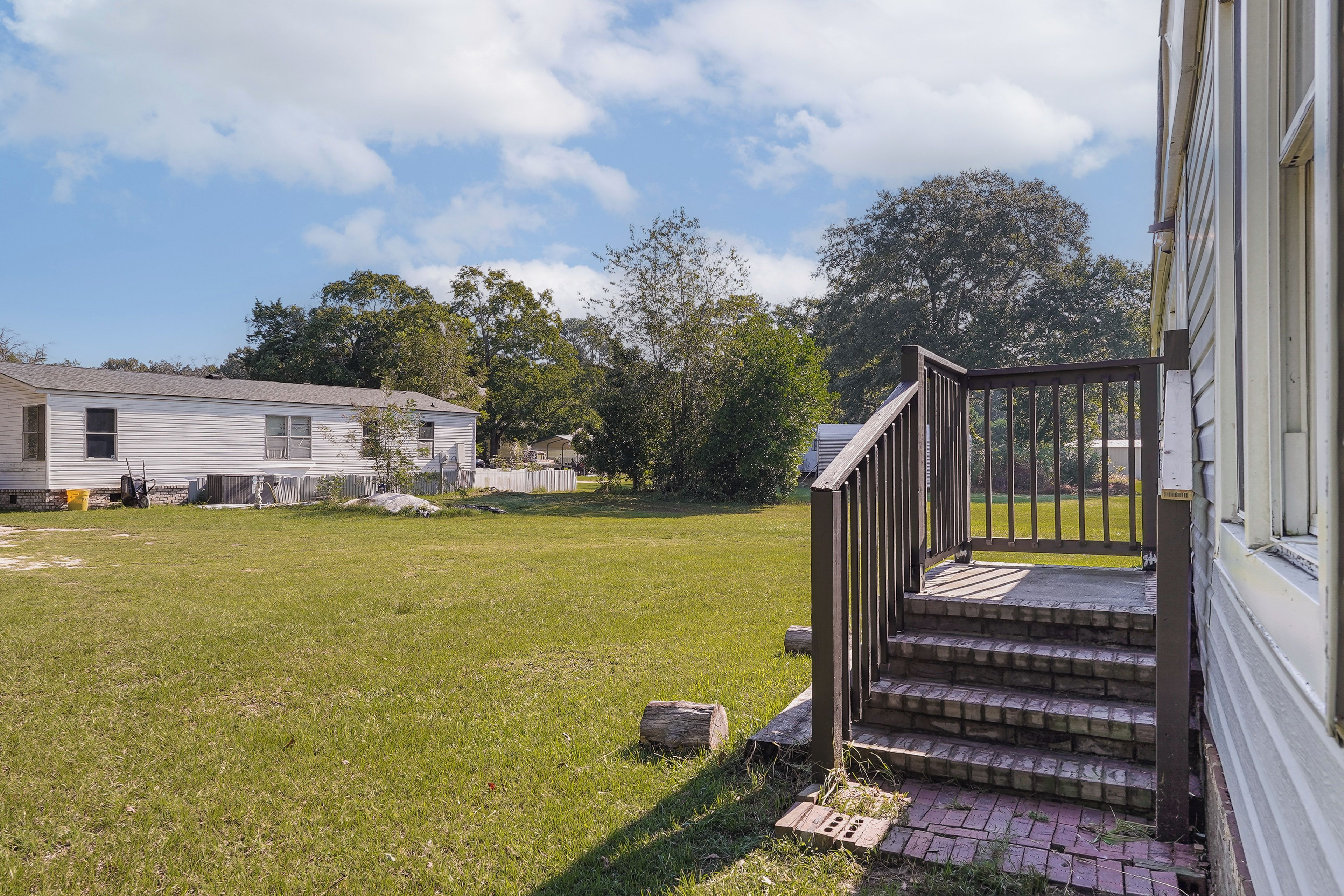 A residential property with a grassy yard, a wooden staircase leading to a porch, and a white building in the background.