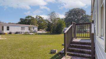 A residential property with a grassy yard, a wooden staircase leading to a porch, and a white building in the background.