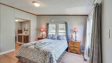 A bedroom with a bed, two bedside tables with lamps, a window with curtains, a mirror, and a wooden dresser.