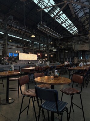 An industrial-style café with high ceilings, exposed beams, and a large windowed skylight. Tables and chairs are arranged for dining. - Stylish and Cozy Waterloo Apartment with Balcony (Waterloo)