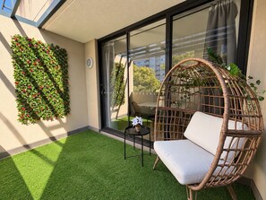 Ein Balkon mit Kunstgrasanlage, einem Korbstuhl, einem kleinen Tisch und einer wandmontierten Pflanzenanordnung.
