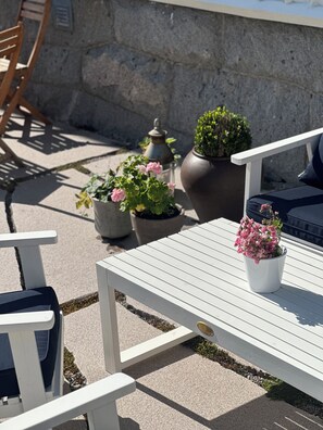 Un área de patio con una mesa blanca, sillas y plantas en macetas.