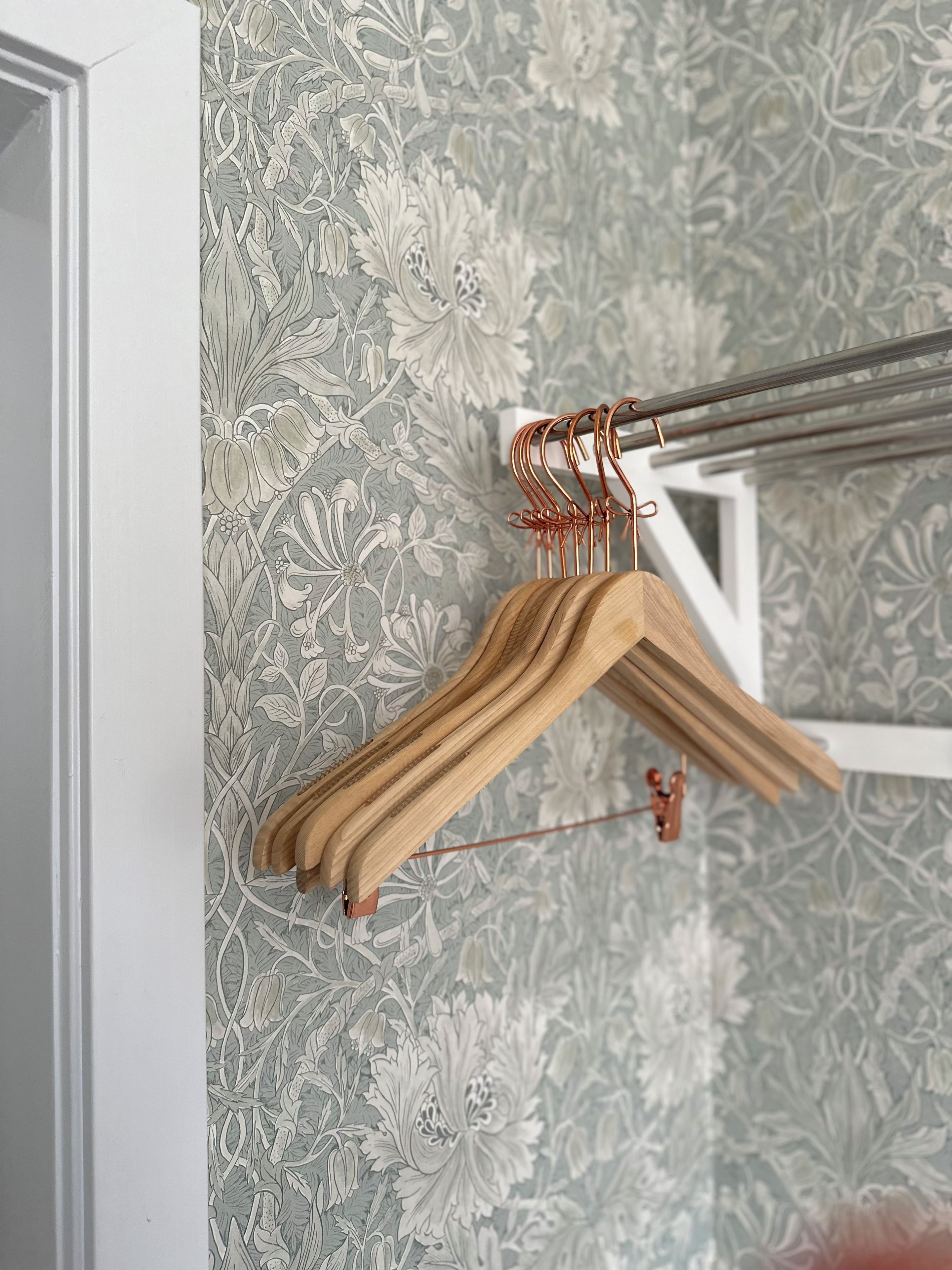 Un perchero de madera con un colgador de alambre de cobre sobre un papel tapiz con motivos florales.