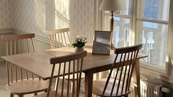 Un coin repas avec une table et des chaises en bois, un certificat encadré, une plante en pot et une fenêtre donnant sur des immeubles.