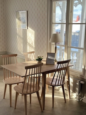 A dining area with a wooden table and chairs, a framed certificate, a potted plant, and a window with a view of buildings.
