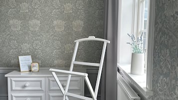 A room with a radiator, a white dresser with drawers, a framed certificate, and a white ladder leaning against the wall.