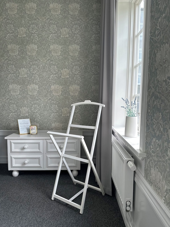 A room with a radiator, a white dresser with drawers, a framed certificate, and a white ladder leaning against the wall.