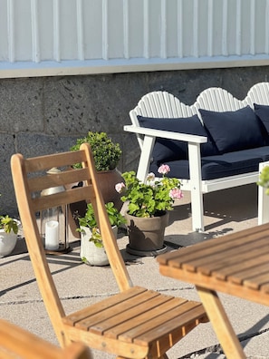 A seating area with wooden chairs and a table, surrounded by potted plants and a white wall.