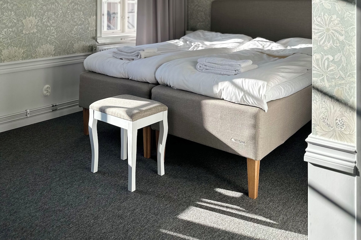 Un dormitorio con una cama grande, una mesita pequeña y un ventanal con cortinas.
