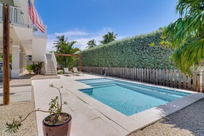 A swimming pool with a wooden deck, a pergola, and a view of a residential building with an American flag. - Private Dock & Pool: Waterfront Key Largo Home (Key Largo)