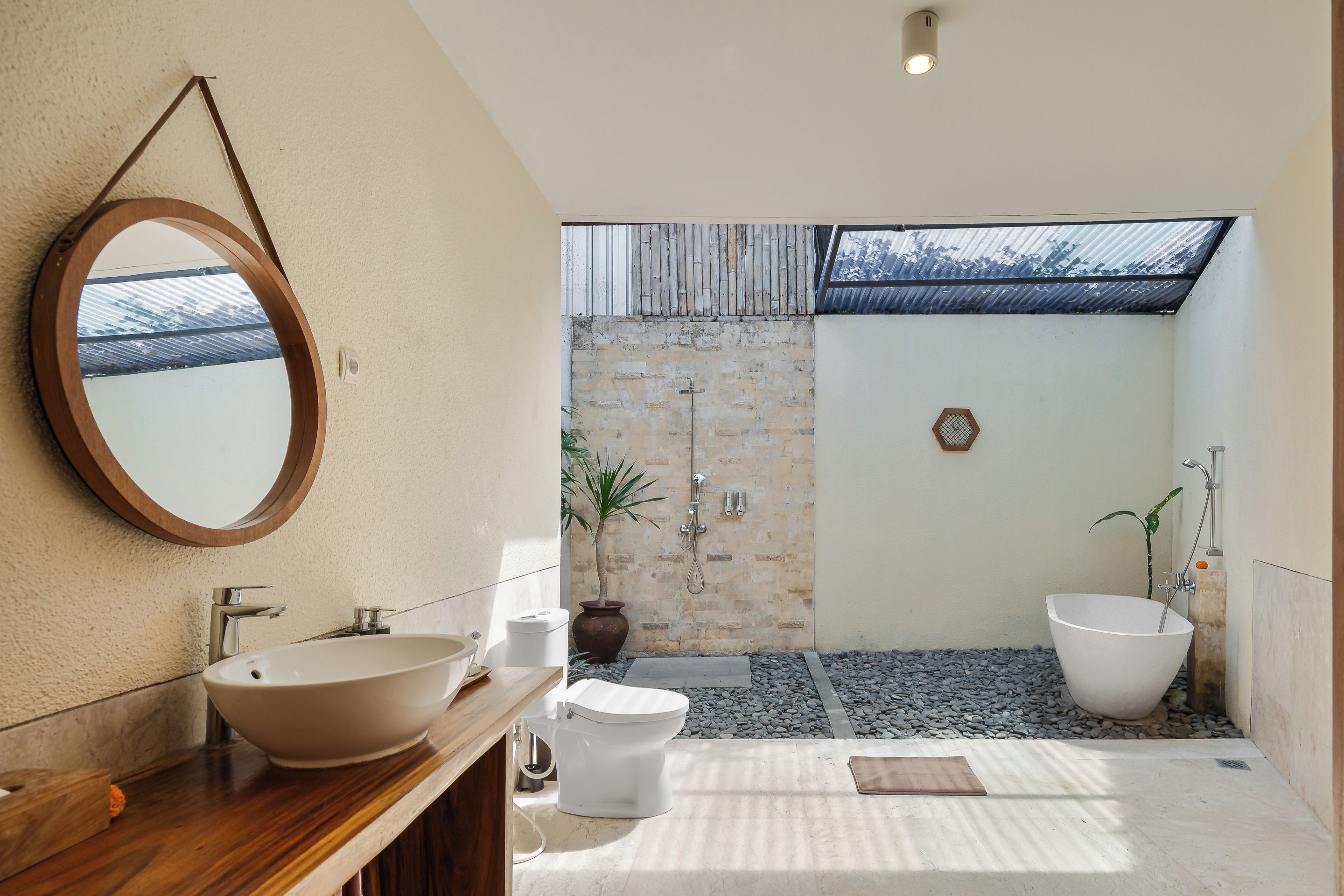 A bathroom with a wooden vanity, a large mirror, a freestanding sink, a toilet, and a shower area with a view of the outside.