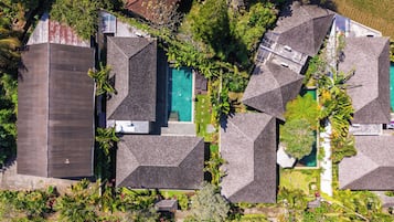Vista aérea de un barrio residencial con varias casas, cada una con un diseño de techo diferente, rodeado de vegetación exuberante y una piscina.