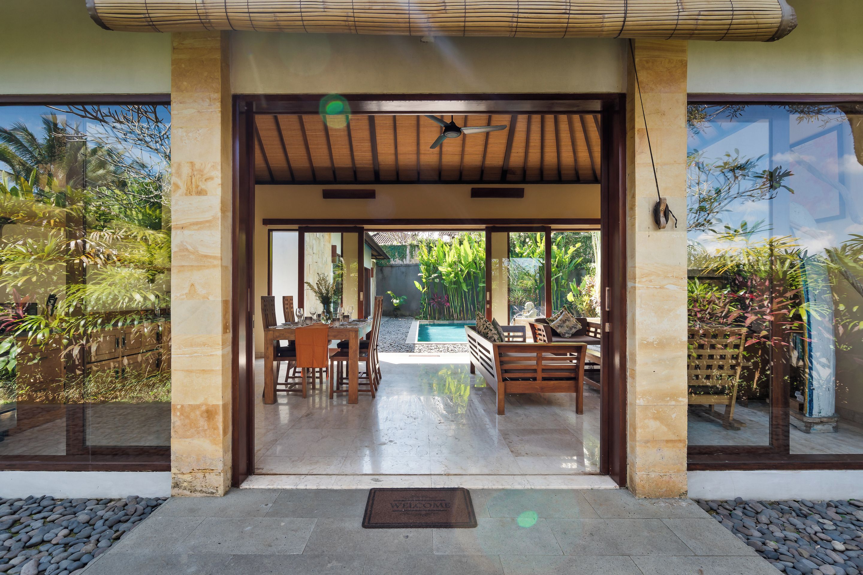 Una entrada moderna a un edificio con un patio cubierto, piscina y abundante vegetación.