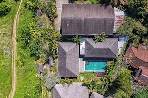 Luchtbeeld van een woonhuis met zwembad, meerdere daken en weelderige begroeiing.
