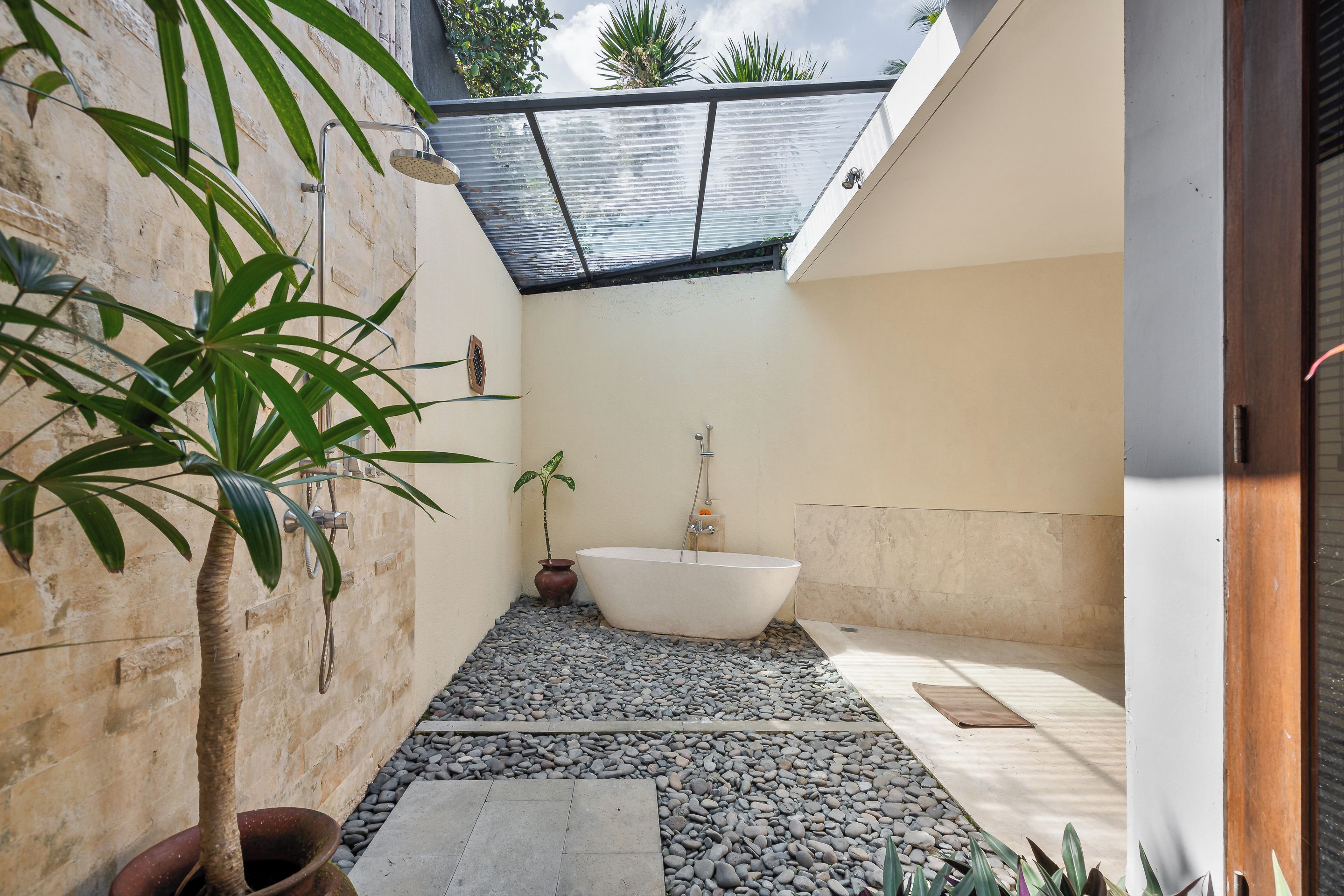 Un baño pequeño y privado con una bañera independiente, una planta en maceta y suelo de baldosas de piedra.