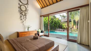 Un dormitorio con una cama grande, un aparador de madera, un atrapasueños y vistas a una piscina y jardín.