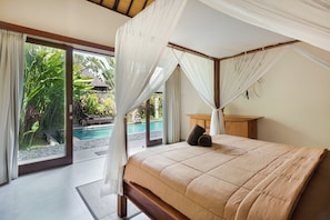 Een slaapkamer met een hemelbed, uitzicht op een zwembad en een tropische tuin.