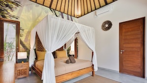 Uma cama de dossel com estrutura de madeira e cortinas brancas, uma mesa de cabeceira com abajur, e uma porta com painel de madeira.