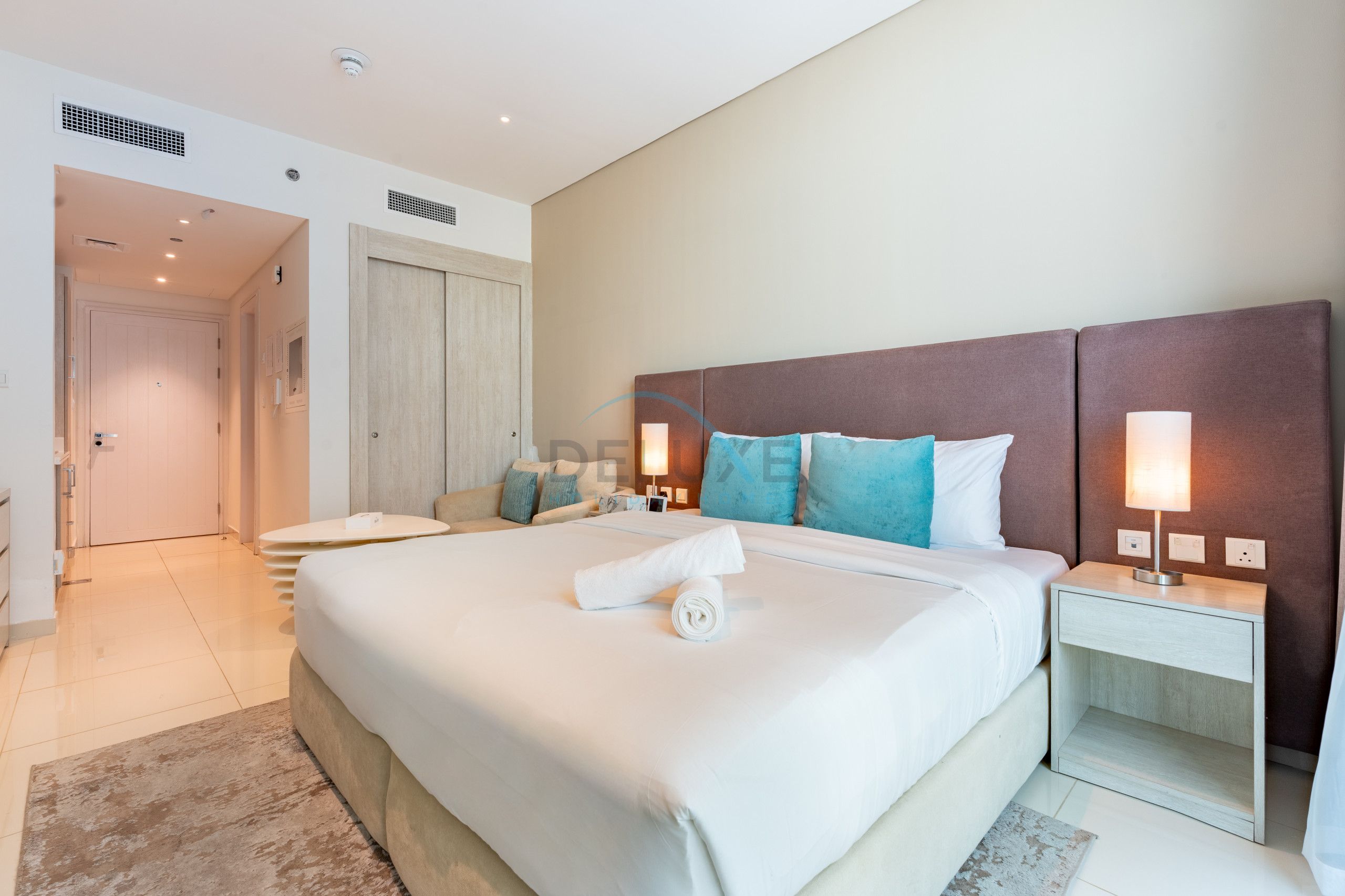 A hotel room with a large bed, bedside tables, a nightstand, a lamp, and a bathroom visible through an open door.