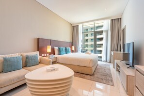 A modern hotel room with a bed, a sofa, a coffee table, and a television. - Neat Studio, Near the Monorail, Nakheel Mall and a Short Ride to Atlantis (Dubai)