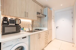 A modern kitchen with a washing machine, a coffee maker, and a kettle. - Neat Studio, Near the Monorail, Nakheel Mall and a Short Ride to Atlantis (Dubai)