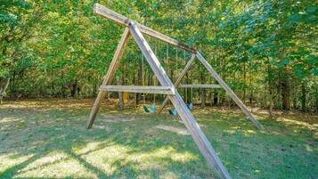 A wooden swing set in a grassy area with trees in the background.