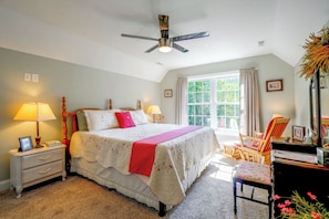 Quarto com cama, abajures, mesa de cabeceira, cadeira, escrivaninha e janela com cortinas.