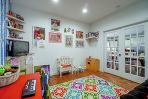 Un cuarto de juegos infantil con televisión, juguetes y una alfombra colorida.