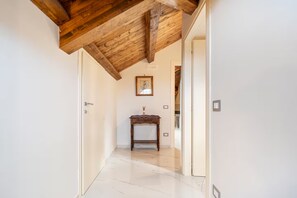 Un couloir avec un plafond en bois, une porte blanche, une petite table sur laquelle se trouve un vase, et un tableau encadré accroché au mur.