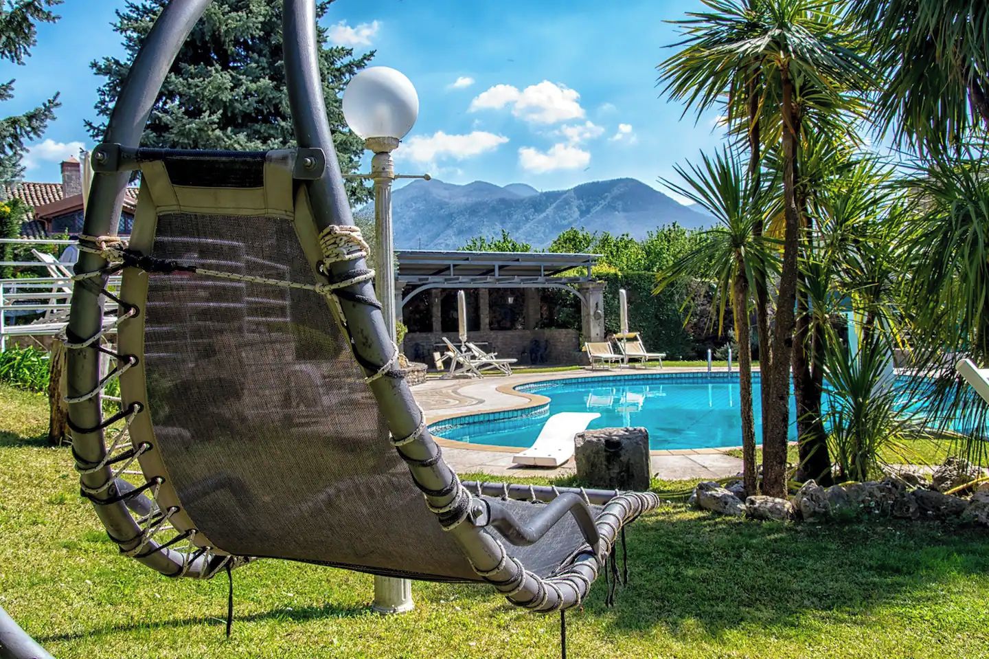 A hammock chair with a view of a swimming pool and mountains in the background.