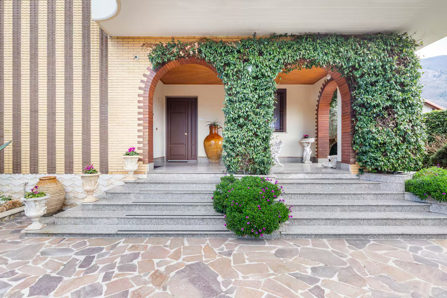 Un ingresso con una scalinata in pietra, un vaso grande e una statua.