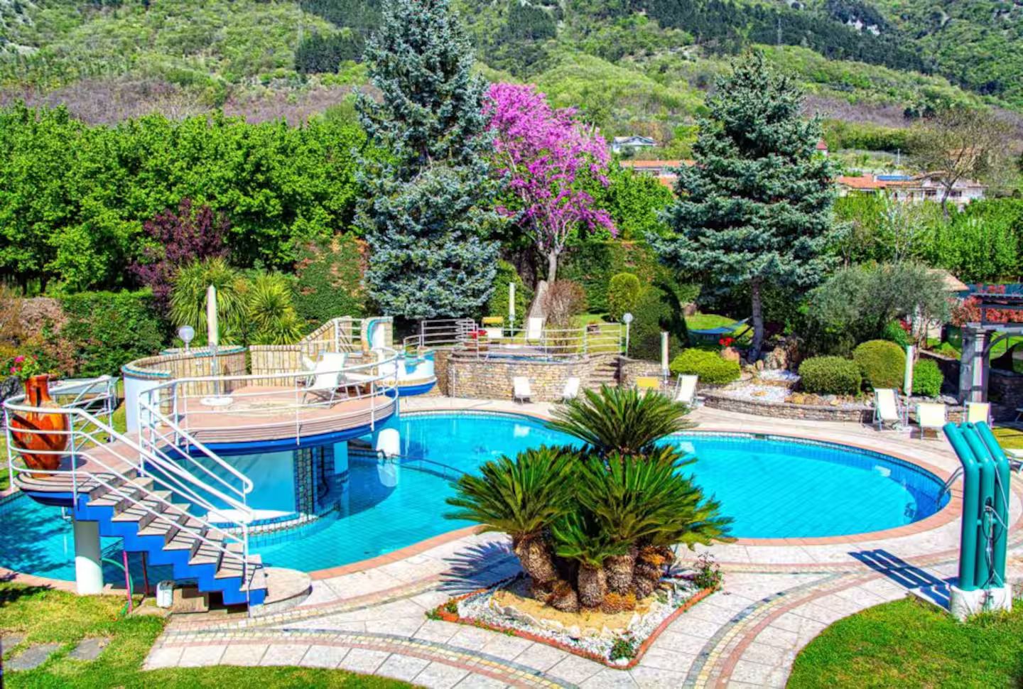 Una piscina con un solarium circostante, scale e una palma.