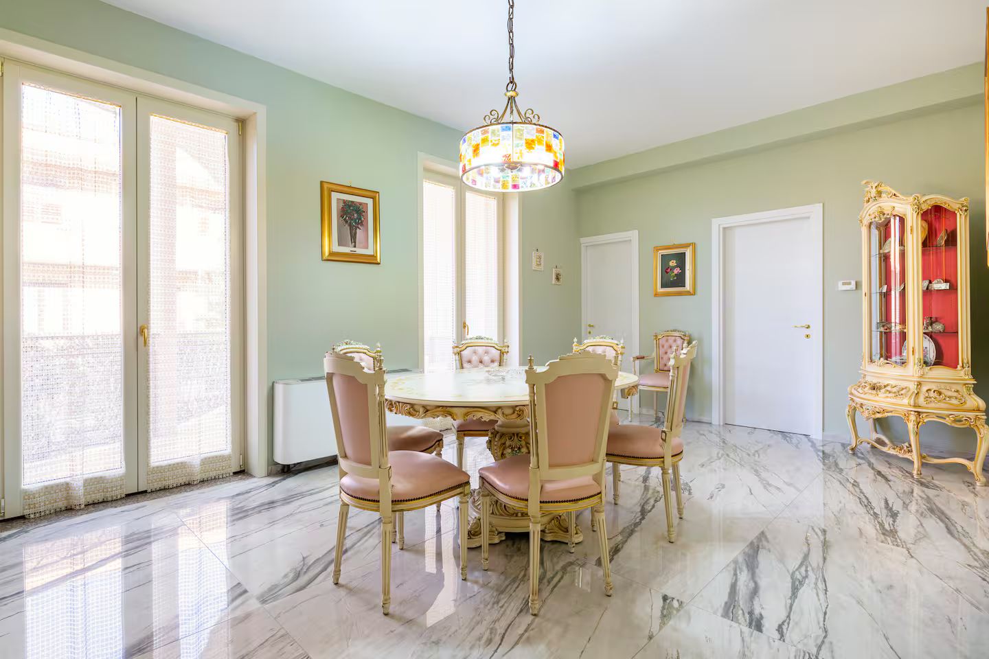 A dining room with a marble floor, a chandelier, and a red cabinet.