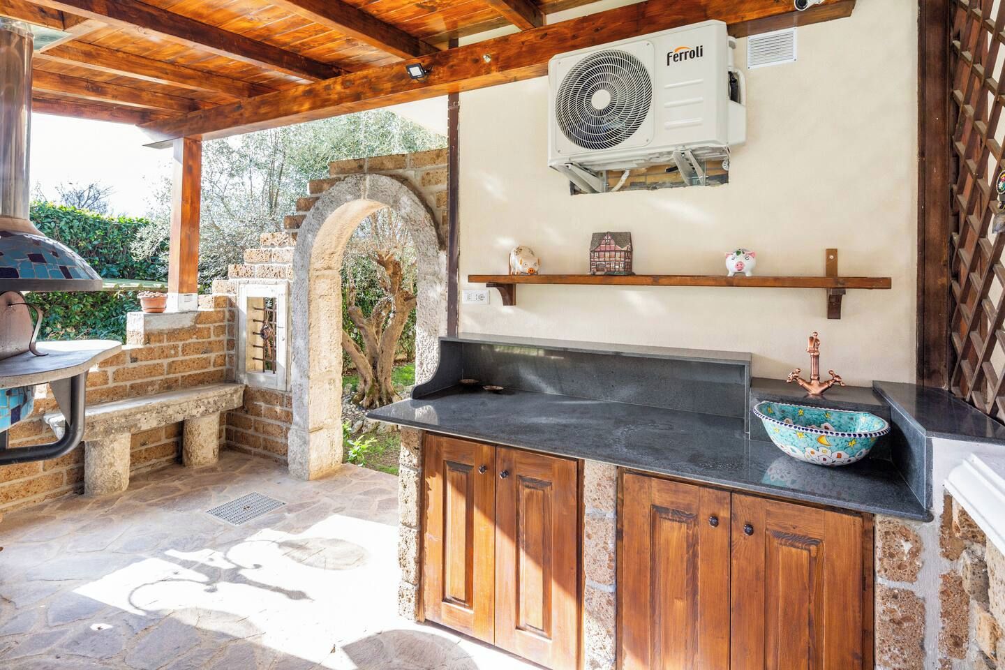 An outdoor kitchen area with a stone archway, a grill, and a built-in sink with a decorative bowl.