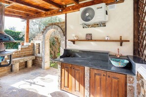 Un espace cuisine extérieur doté d’une arche en pierre, d’un barbecue et d’un évier encastré agrémenté d’un récipient décoratif.