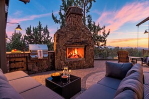 A stone fireplace with a fire, outdoor seating, and a view of the sky. - Spacious 6700 SQFT Home | 4 Ensuite Bedrms + Kids Bunkrm + Game Rm + Media Room (Powell Butte)